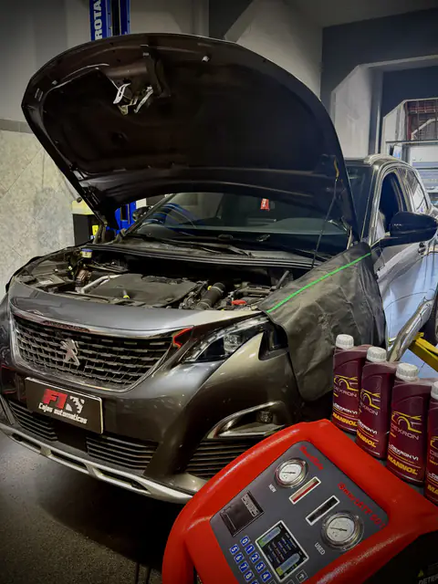 Peugeot gris con capó abierto y cubreguardabarros, botellas de ATF Mannol Dexron VI y equipo de diálisis