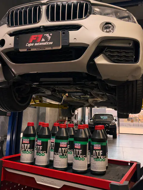 BMW blanco en el elevador con chapa F1 y botellas de ATF Liqui Moly Top Tec 1800 sobre carro Würth