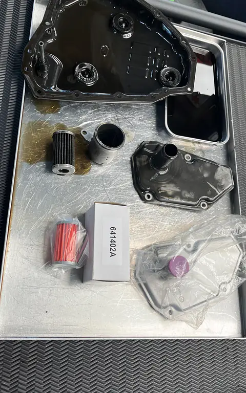 Cárter, filtros usados y repuestos embolsados con su caja, sobre bandeja metálica con restos de aceite