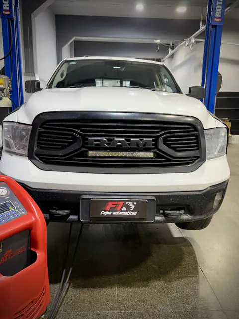 Pickup RAM blanca con chapa F1 entre las columnas del elevador, con el equipo de diálisis al costado