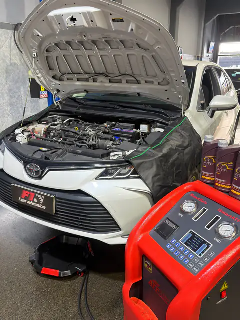 Toyota blanco con capó abierto y chapa F1, con el equipo iSmartATF y botellas de ATF Mannol encima