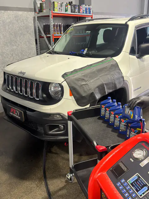 Jeep blanco con cubreguardabarros, mano con guante y carro con botellas Valvoline, junto al equipo de diálisis
