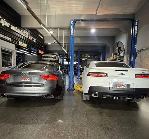 Audi RS5 y Chevrolet Camaro lado a lado en el taller, entre elevadores y carteles de marcas
