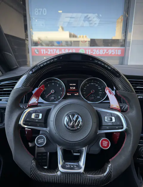 Volante Volkswagen GTI de fibra de carbono con levas rojas; al fondo, la vidriera del local