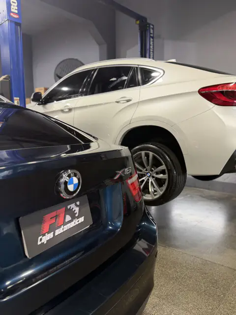 Detalle del emblema BMW y la placa de Cajas Automáticas F1 de un X6 azul, con otro X6 blanco elevado detrás