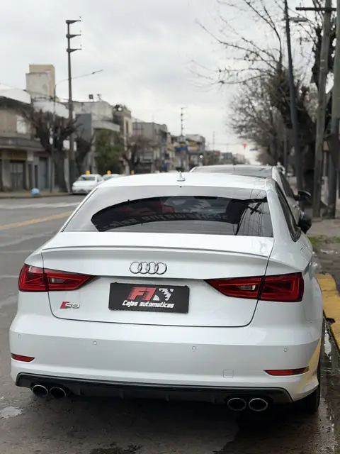 Audi S3 blanco visto desde atrás con la placa de F1, estacionado junto al cordón amarillo