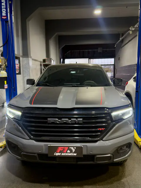 Pickup RAM gris con franjas negras en el capó, de frente entre las columnas de un elevador