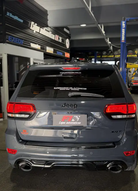 Jeep SRT gris visto desde atrás dentro del taller, con elevadores y carteles de marcas al fondo