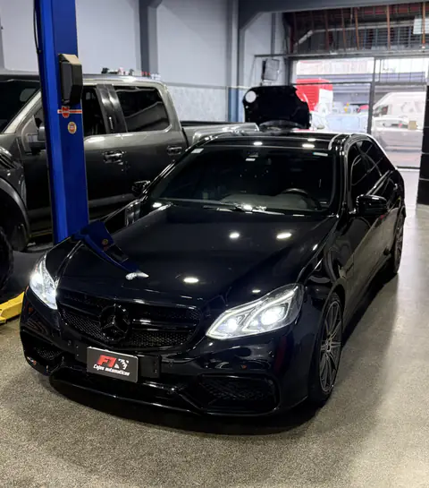 Mercedes-Benz negro de frente con faros encendidos, junto a la columna de un elevador