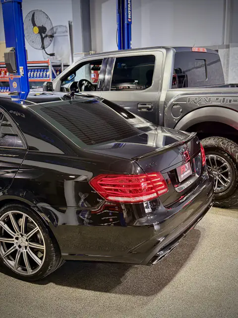 Mercedes-Benz E63 negro en el taller, junto a una pickup Ford Raptor gris