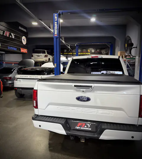 Ford F-150 blanca con cobertor de caja en el taller, junto a una Range Rover y elevadores