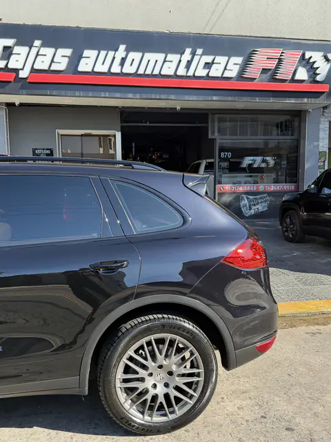 Porsche Cayenne oscura de perfil frente al local, con el cartel de Cajas Automáticas F1 arriba