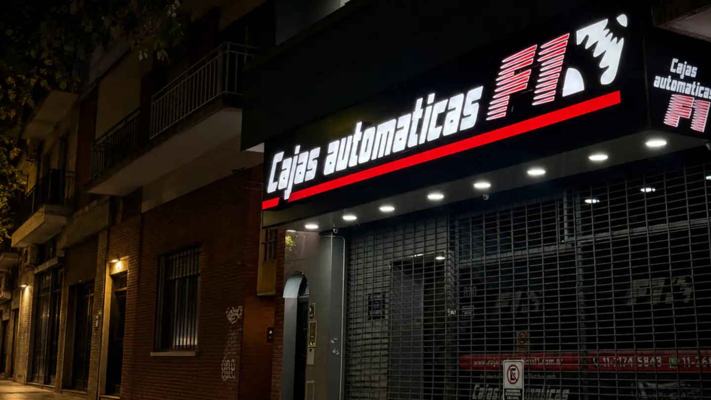 Fachada nocturna del taller Cajas Automáticas F1, con el cartel iluminado sobre la persiana