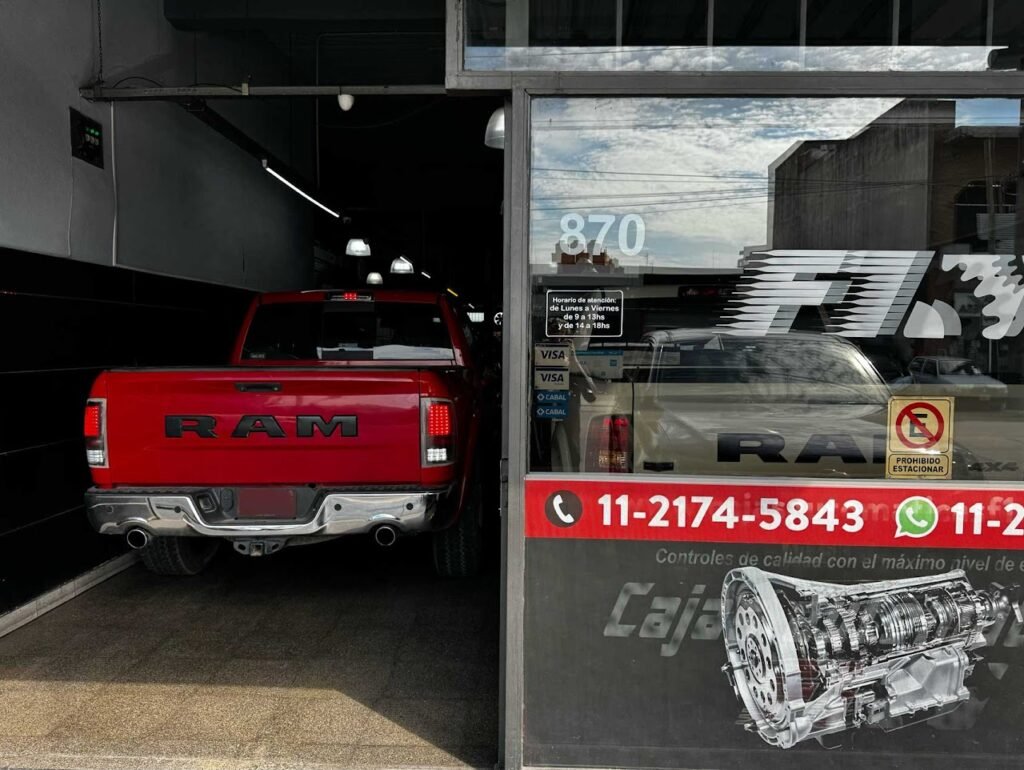 Camioneta RAM roja en el ingreso del taller, junto al cartel con los teléfonos de F1