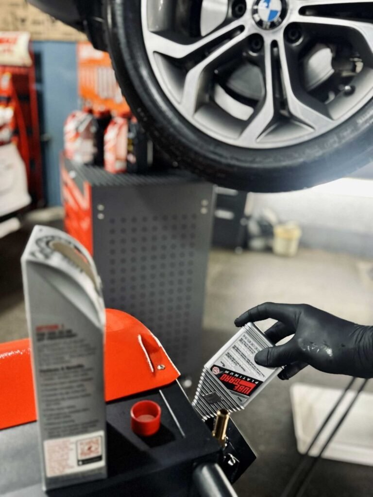 Técnico con guantes cargando fluido de transmisión debajo de un auto elevado