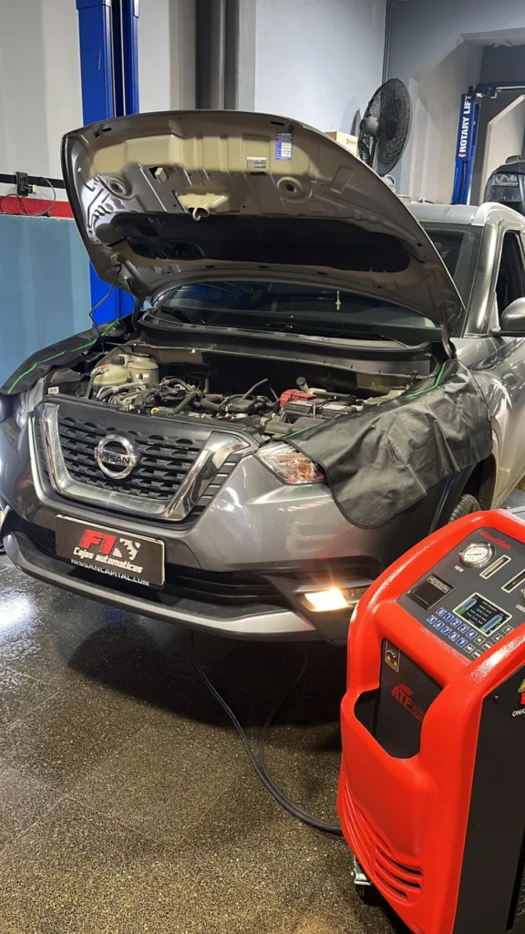 Nissan gris con el capó abierto, conectado a un equipo para el servicio de la transmisión