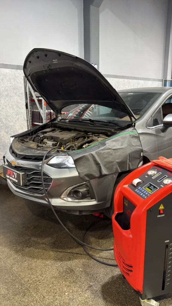 Chevrolet gris con el capó abierto junto a un equipo para el servicio de la transmisión